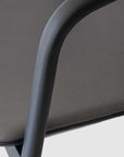 Close-up of the Wooden Stories Inlay Dining Chair in black oak and leather, showing its textured taupe seat and smooth, curved solid wood arms against a light gray background.