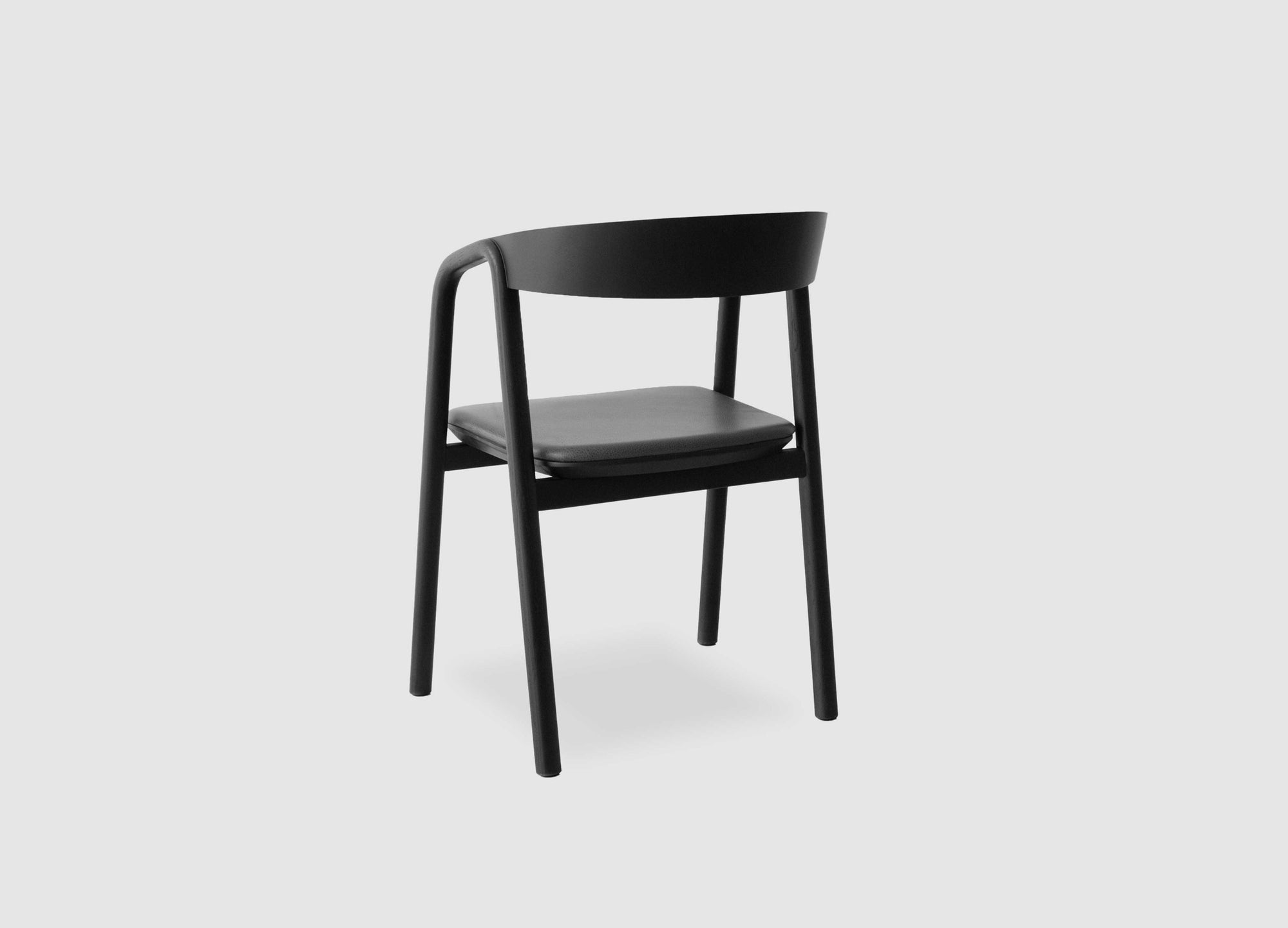 The Wooden Stories Inlay Dining Chair in black oak and leather features a curved plywood backrest, four straight legs, and a flat seat, offering a sleek, minimalist look against a plain light gray background.