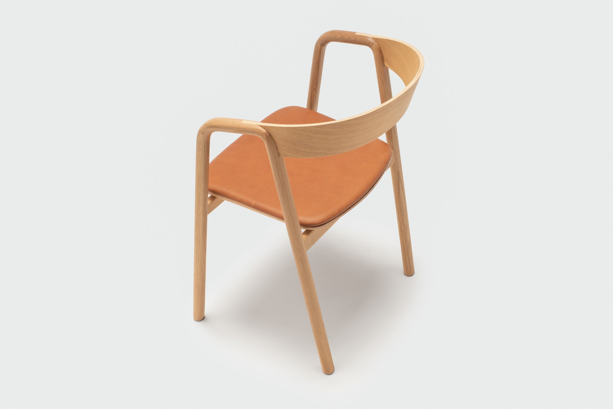 The Wooden Stories Inlay Dining Chair features a curved light oak plywood backrest, armrests, and a tan leather upholstered seat, set against a plain white background.