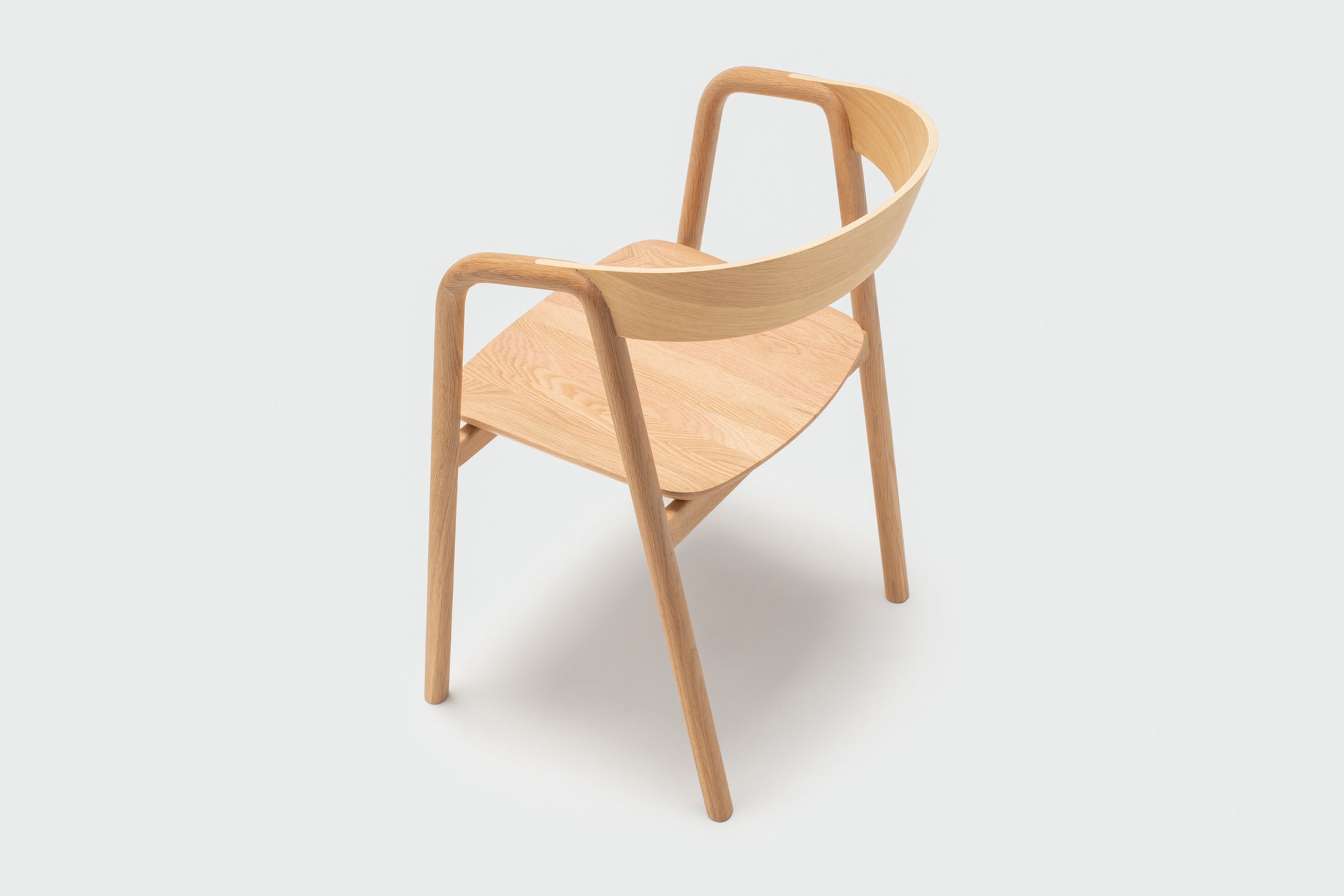 The Inlay Dining Chair | Light Oak by Wooden Stories features a curved plywood backrest and seat with smooth, rounded edges and angled legs, shown against a plain light-gray background.