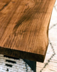 Close-up of the Moes Leviathan Live Edge Coffee Table, highlighting its polished solid acacia surface and unique wood grain; a patterned rug contrasts in the blurred background.