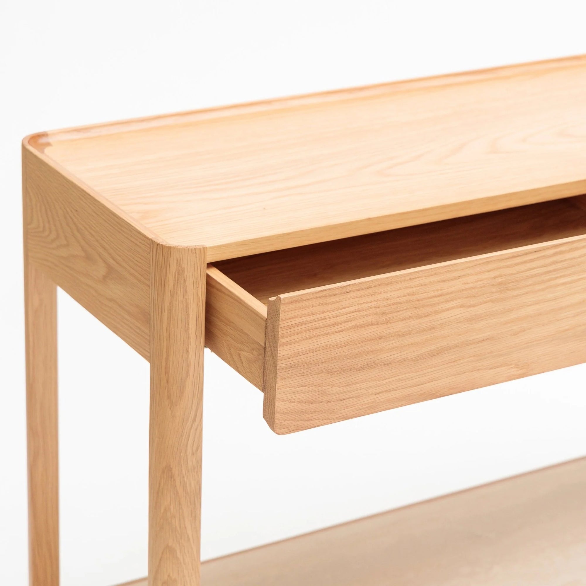 The Nell Console by Wooden Stories showcases minimalist Danish-inspired design in light oak, featuring clean lines, a smooth surface, and a single partially open drawer, all highlighted by its natural wood finish.