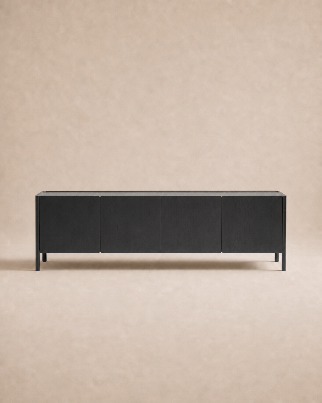 A modern Nell Sideboard | Black Oak by Wooden Stories, featuring four doors and a minimalist Scandinavian-inspired design with clean lines and handle-free fronts, sits against a light beige, textured background.