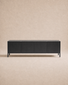 A modern Nell Sideboard | Black Oak by Wooden Stories, featuring four doors and a minimalist Scandinavian-inspired design with clean lines and handle-free fronts, sits against a light beige, textured background.