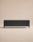 A modern Nell Sideboard | Black Oak by Wooden Stories, featuring four doors and a minimalist Scandinavian-inspired design with clean lines and handle-free fronts, sits against a light beige, textured background.