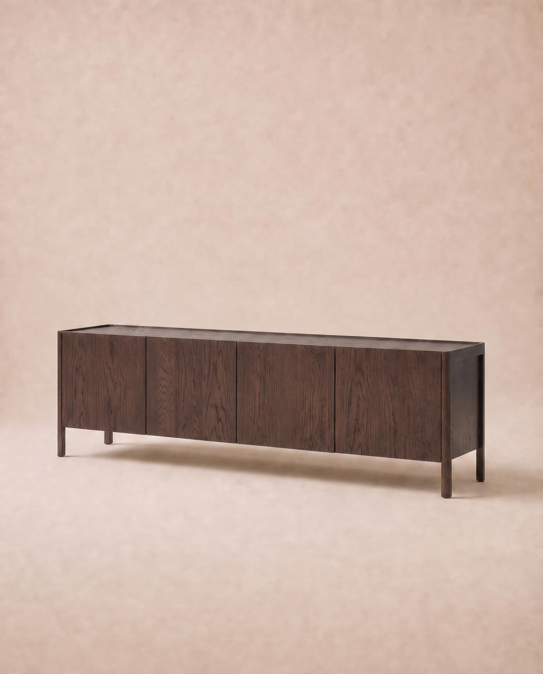 A long, rectangular Nell Sideboard in Espresso Oak by Wooden Stories, featuring four doors and simple legs that embody Scandinavian design, is set against a soft beige background.