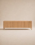 The Wooden Stories Nell Sideboard | Light Oak features four doors, clean lines, and a light natural solid oak finish that embodies Scandinavian minimalism. It is showcased against a beige background.