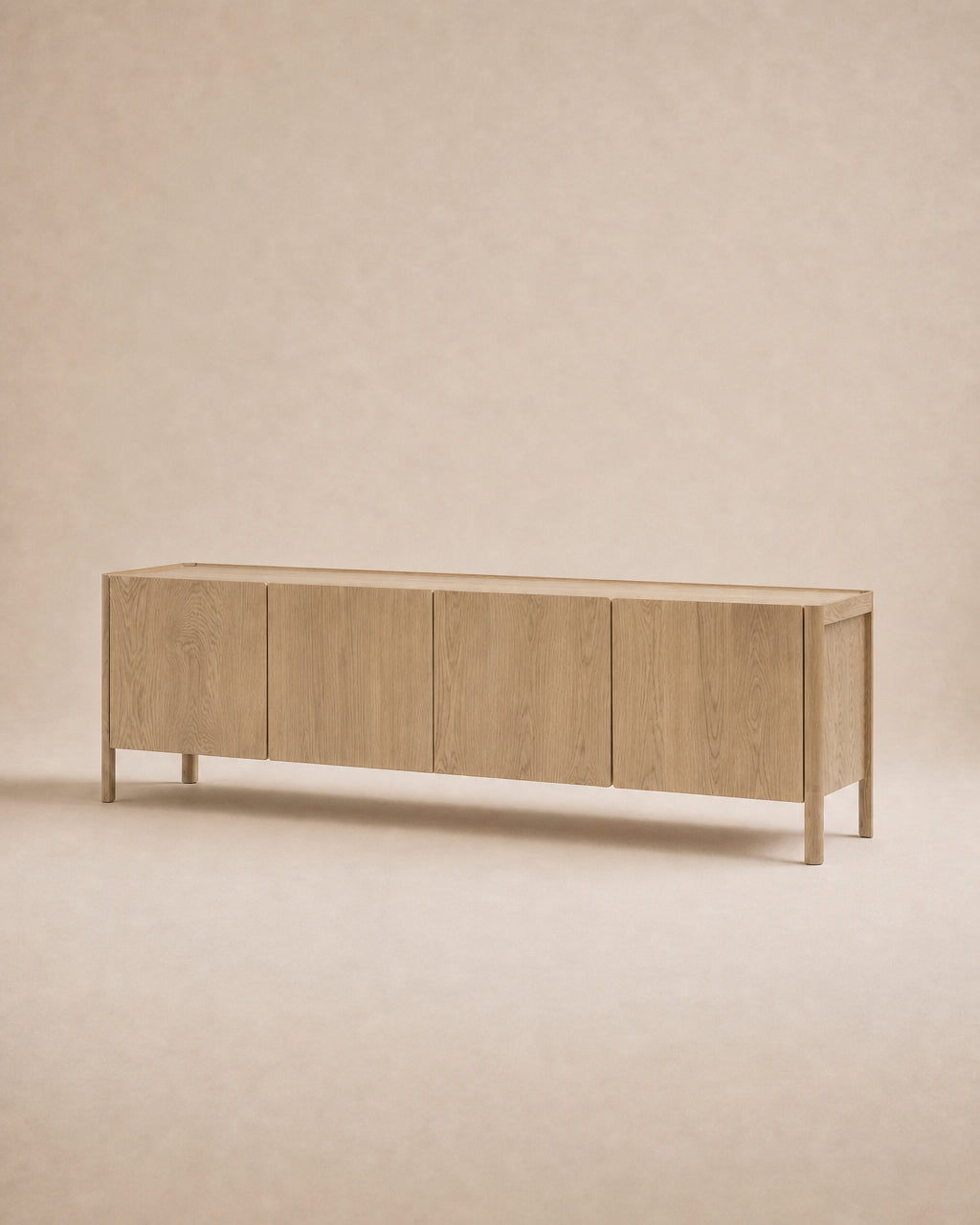 The Nell Sideboard in Blonde Oak by Wooden Stories is a long, solid oak sideboard featuring four cabinet doors, clean lines, and a minimalist design inspired by the Danish collection, showcased against a neutral beige background.