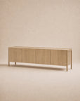 The Nell Sideboard in Blonde Oak by Wooden Stories is a long, solid oak sideboard featuring four cabinet doors, clean lines, and a minimalist design inspired by the Danish collection, showcased against a neutral beige background.