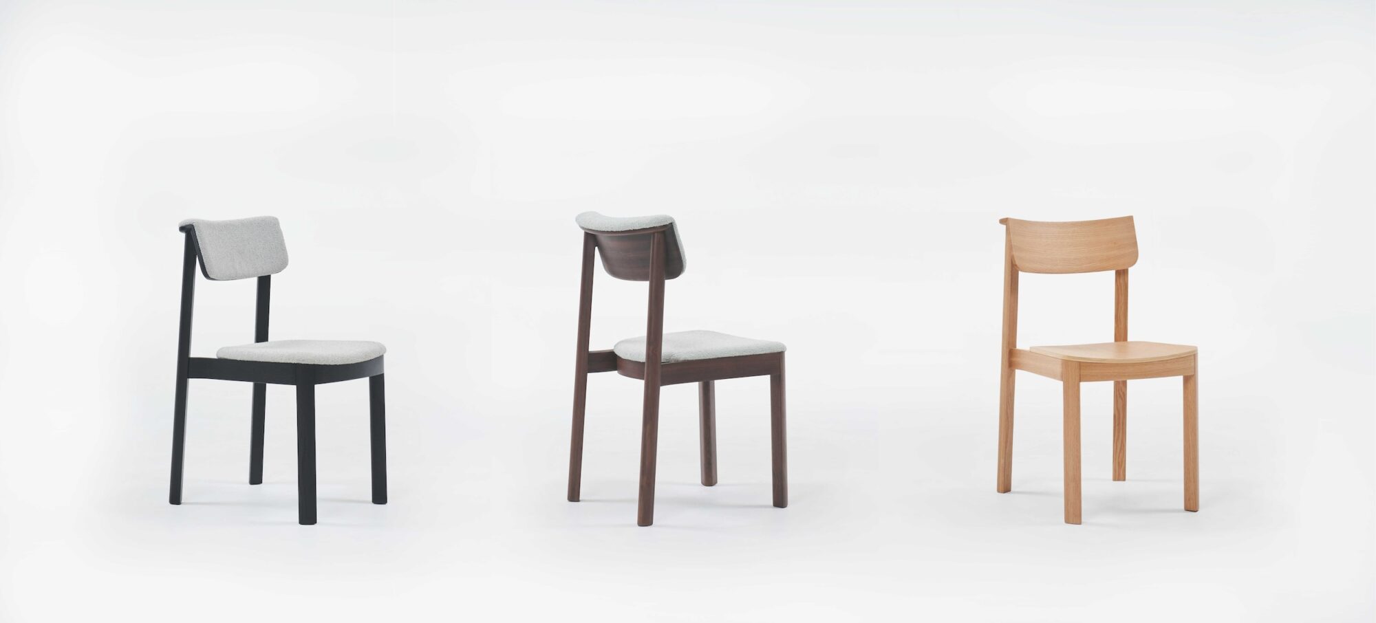 Three Noki Dining Chairs by Wooden Stories, crafted in black oak, are shown in a row on a white background—two with fabric seat and backrest cushions, the third left plain without cushioning.