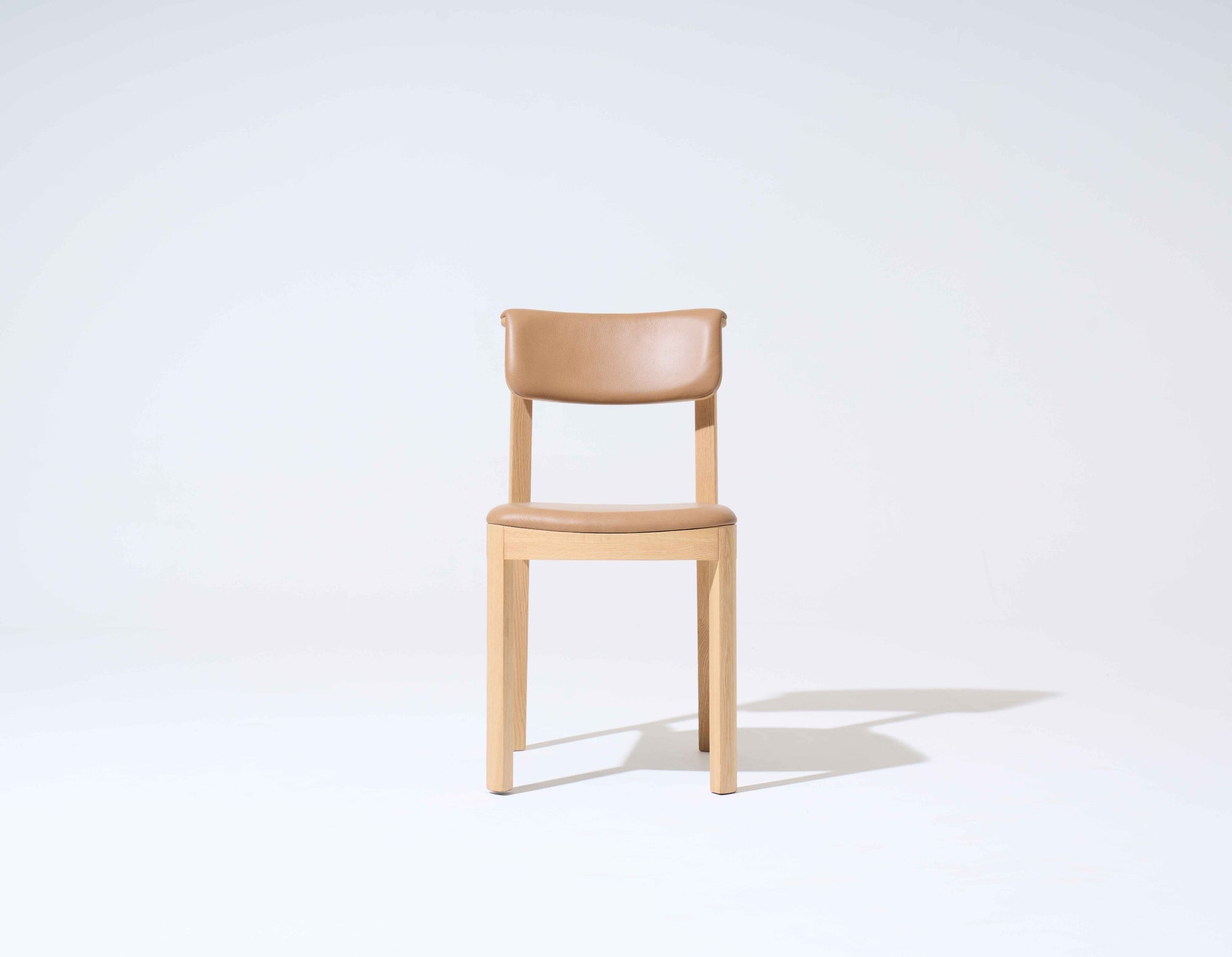 The Wooden Stories Noki Dining Chair features light oak and a curved tan leather seat and backrest. It is set against a plain white background with a faint shadow on the right.