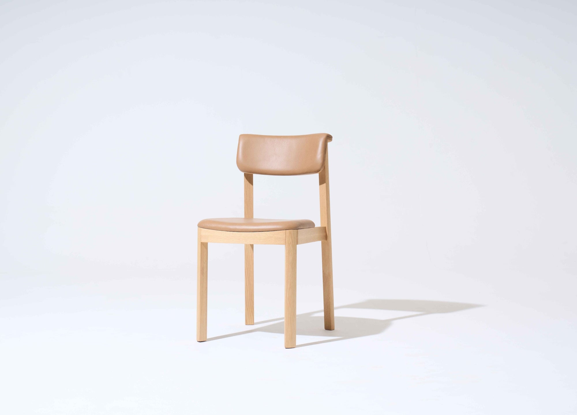 The Noki Dining Chair | Light Oak with Leather by Wooden Stories features a solid wood frame, light brown leather seat and backrest, set against a simple background—ideal for contract-grade interiors.
