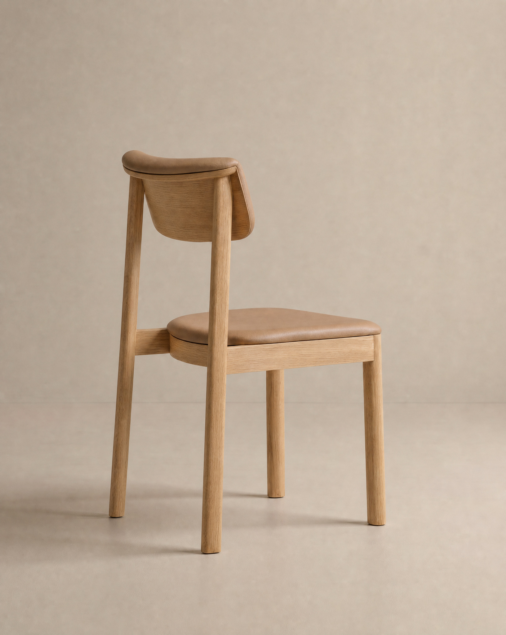 The Noki Dining Chair | Leather by Wooden Stories is a minimalist solid wood chair with a light brown padded leather seat and backrest. Perfect for home or contract use, it’s shown on a neutral background and angled slightly away from the camera.