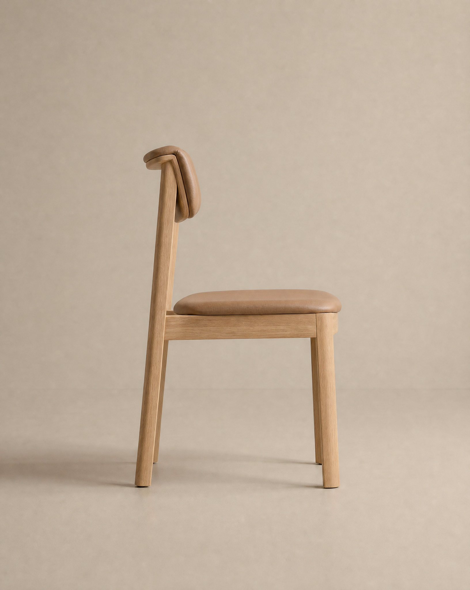 The Noki Dining Chair | Leather by Wooden Stories features a minimalist solid wood design, tan leather seat, and distinctive curved backrest, displayed in profile against a neutral beige background.