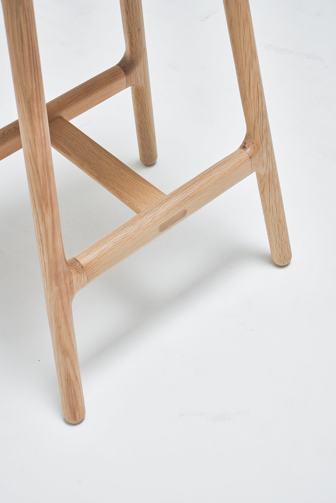 Close-up of the Odd Counter Stool by Wooden Stories, featuring light oak legs with a leather seat. The smooth, rounded edges and visible wood grain reflect true Danish design style, shown on a white background.