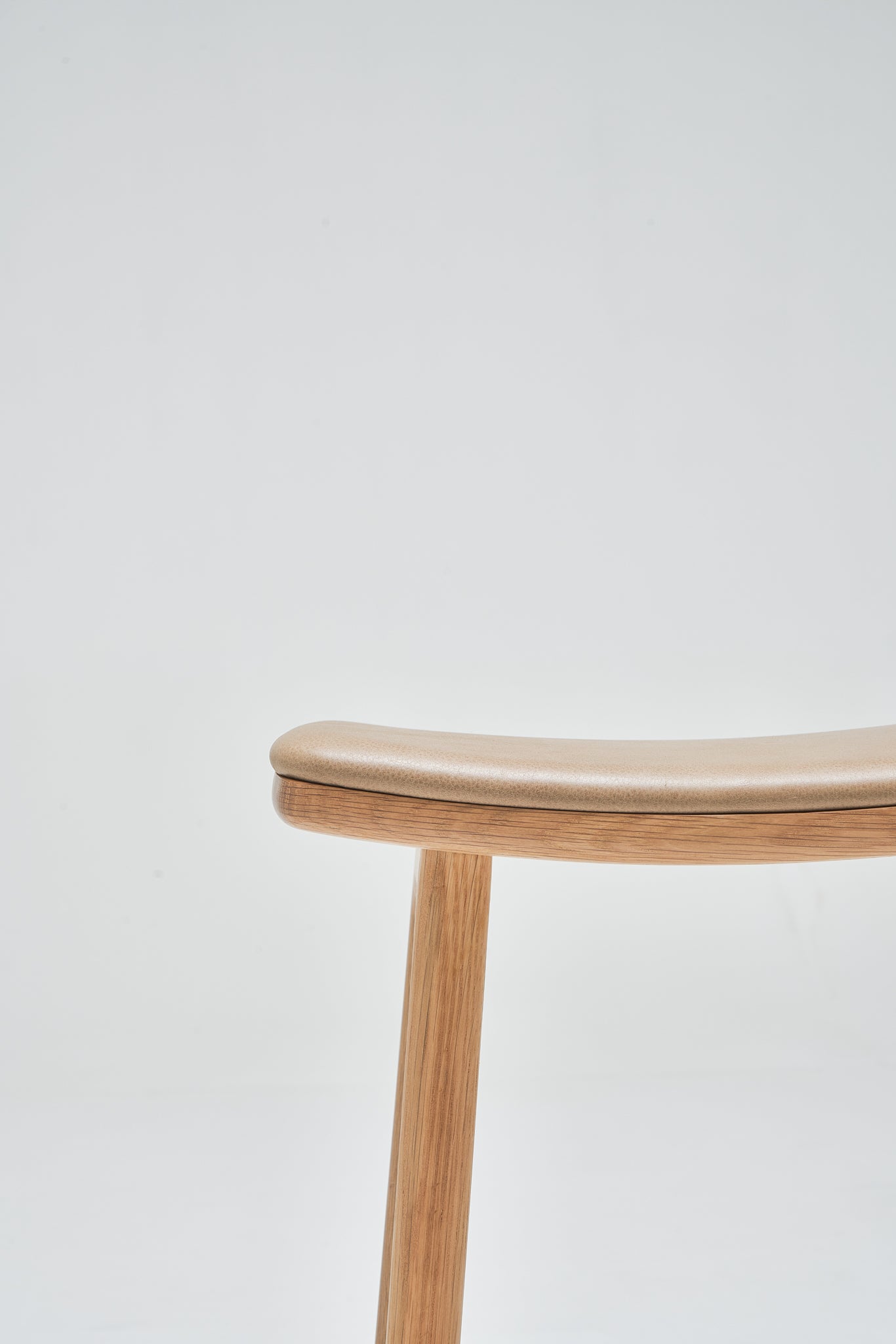 Minimalist photo of the Odd Counter Stool by Wooden Stories, featuring a light oak frame with a leather seat and single visible leg, crafted from natural materials and set against a plain white background for a modern, Danish-inspired look.