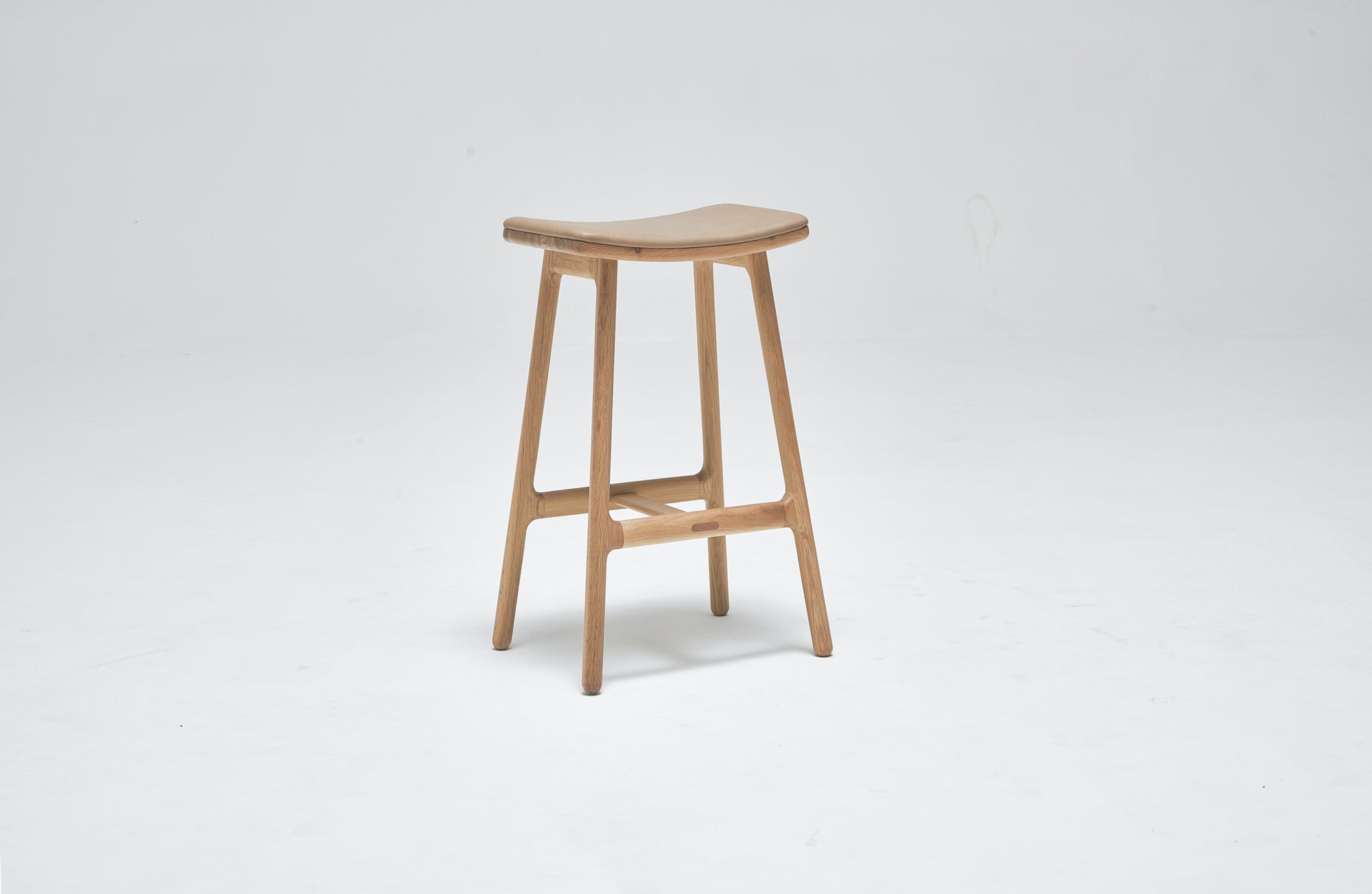 The Odd Counter Stool by Wooden Stories features a light oak frame, a genuine leather seat, and four sturdy legs, showcased against a plain white background.