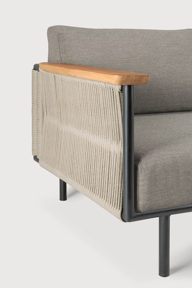 A close-up of Ethnicraft’s Corbey Outdoor Sofa showcases gray cushions, a black metal frame, light wood armrests, and woven beige rope panels—ideal for a stylish outdoor retreat against a plain white background.