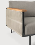 A close-up of Ethnicraft’s Corbey Outdoor Sofa showcases gray cushions, a black metal frame, light wood armrests, and woven beige rope panels—ideal for a stylish outdoor retreat against a plain white background.