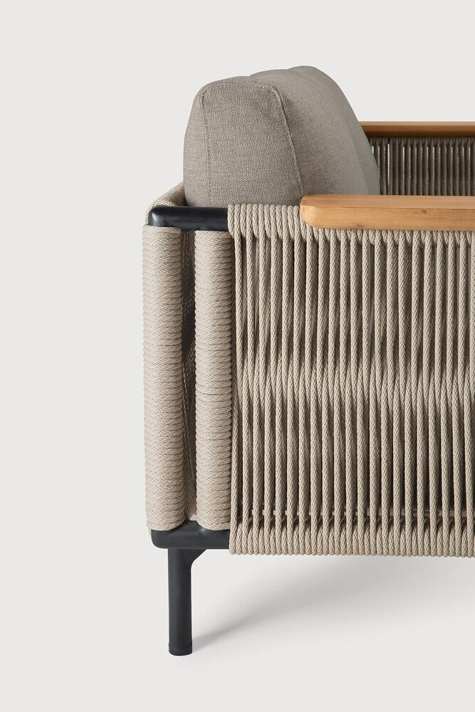 Close-up side view of the Ethnicraft Corbey Outdoor Sofa, showcasing tightly woven beige rope, a black metal frame, wooden armrest accents, and a light gray cushion—an ideal addition to your outdoor space.