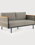 The Corbey Outdoor Sofa by Ethnicraft has light gray cushions, a black metal frame, wooden armrests, and woven rope sides—ideal for crafting an outdoor haven against a plain light background.