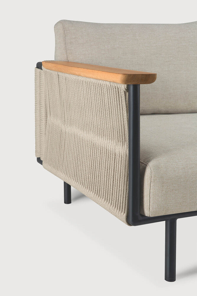 A close-up of the Corbey Outdoor Sofa by Ethnicraft highlights its light wood armrest, black metal frame, beige woven fabric sides, and light beige upholstered seat and back—perfect minimalist elegance for your outdoor space.