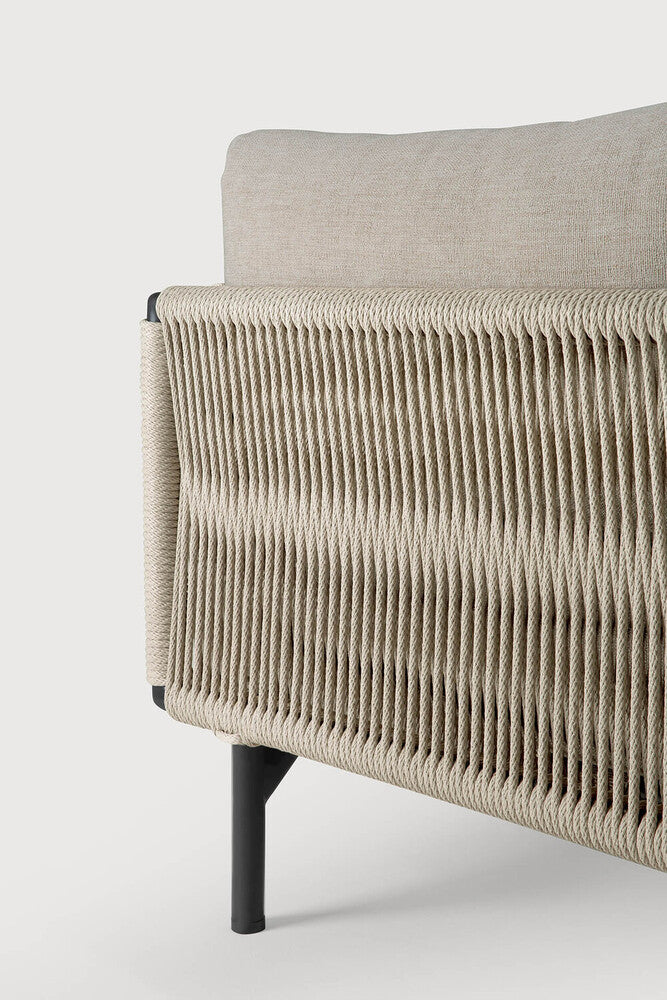 Close-up of the Ethnicraft Corbey Outdoor Sofa, showing a beige cushion and woven rope side panel on black metal legs. This stylish piece creates an inviting outdoor haven against a plain white background.