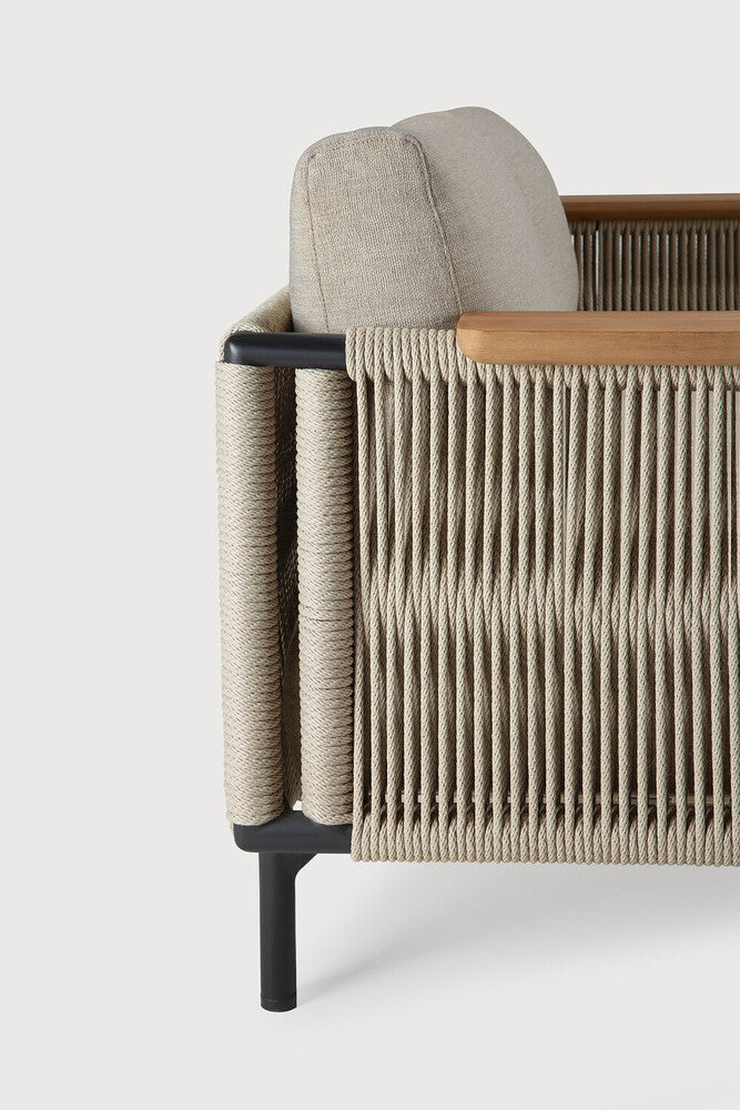 Close-up side view of the Ethnicraft Corbey Outdoor Sofa, showcasing beige woven rope sides, a light beige cushion, light wood armrest, and black metal legs—ideal for an inviting outdoor oasis against a white backdrop.