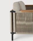 Close-up side view of the Ethnicraft Corbey Outdoor Sofa, showcasing beige woven rope sides, a light beige cushion, light wood armrest, and black metal legs—ideal for an inviting outdoor oasis against a white backdrop.