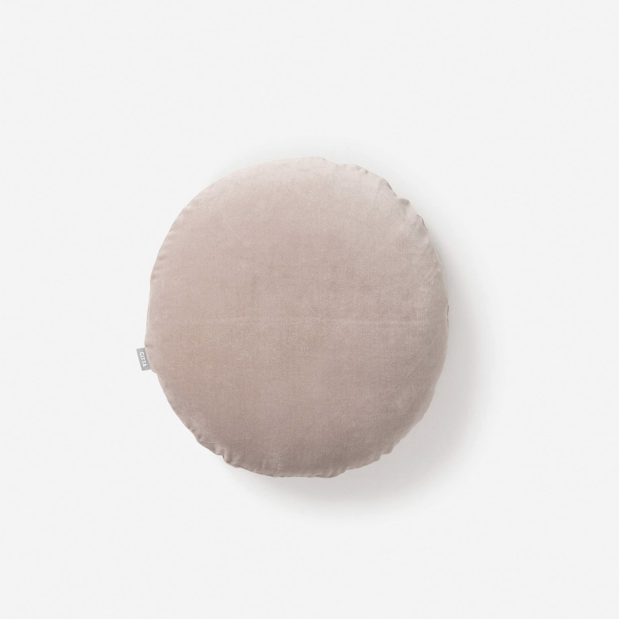 The CITTA Velvet Round Cushion - Scoria Tint features light beige velvet and a small fabric tag on the left, styled against a plain white background—a cozy New Zealand accent.