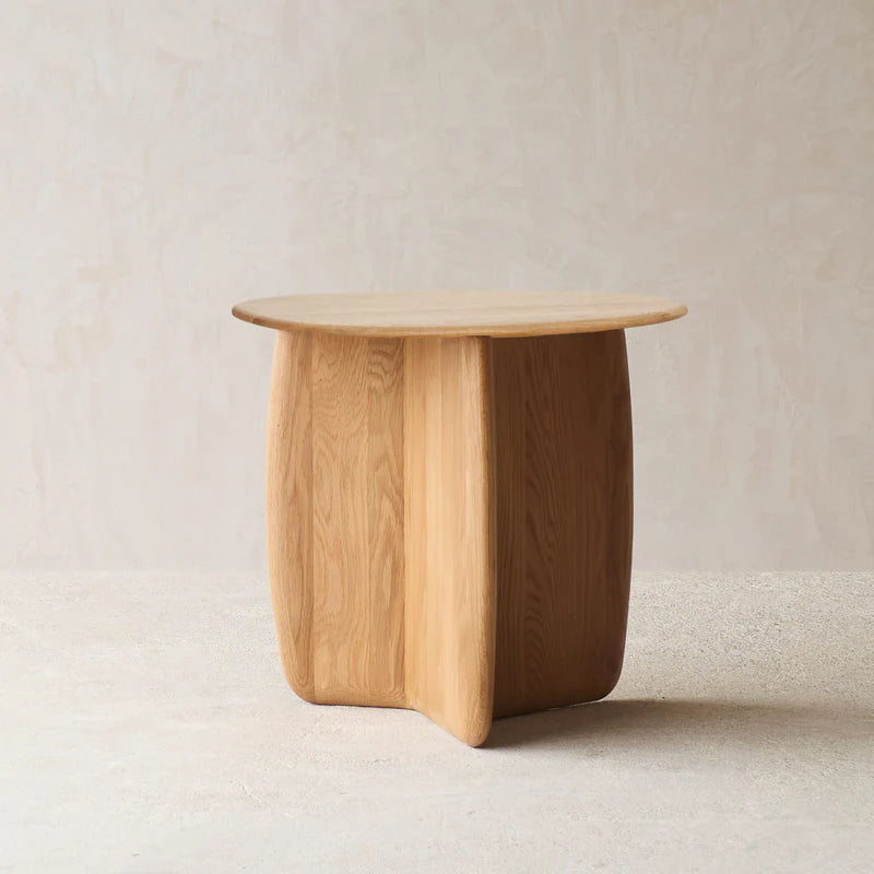 The Eden Side Table - Light Oak by Wooden Stories features a smooth, round top and sculptural base, adding organic elegance to any sophisticated interior with its neutral beige tones.