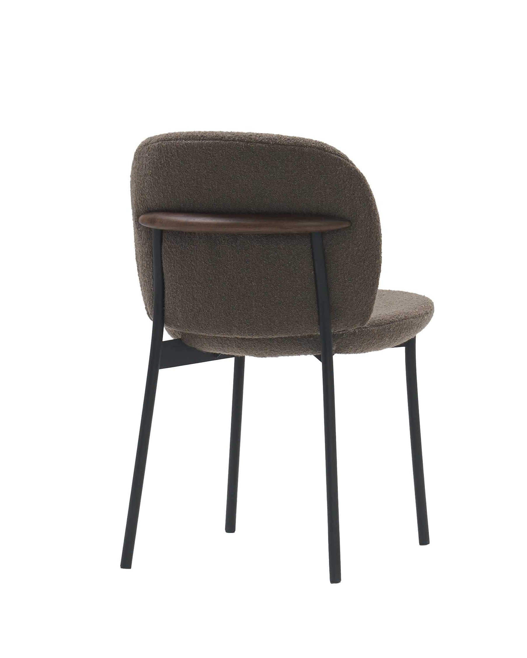 The Solace Dining Chair | Fabric by Wooden Stories is a modern upholstered dining chair with a rounded brown seat and backrest, slim black metal legs, and a wood accent on the upper backrest, shown against a white background.