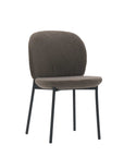 The Solace Dining Chair by Wooden Stories features a modern design with a rounded, cushioned seat and backrest in dark fabric and four slender black metal legs, shown isolated on a white background.