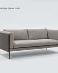 A modern gray three-seater Sonder Sofa | Fabric by Wooden Stories, featuring textured fabric feather-filled cushions, slim black legs, and dark wooden side panels, is set against a plain white background. Its subtle Danish lines and linear frame enhance the contemporary appeal. Text in the corner notes the model name and availability.