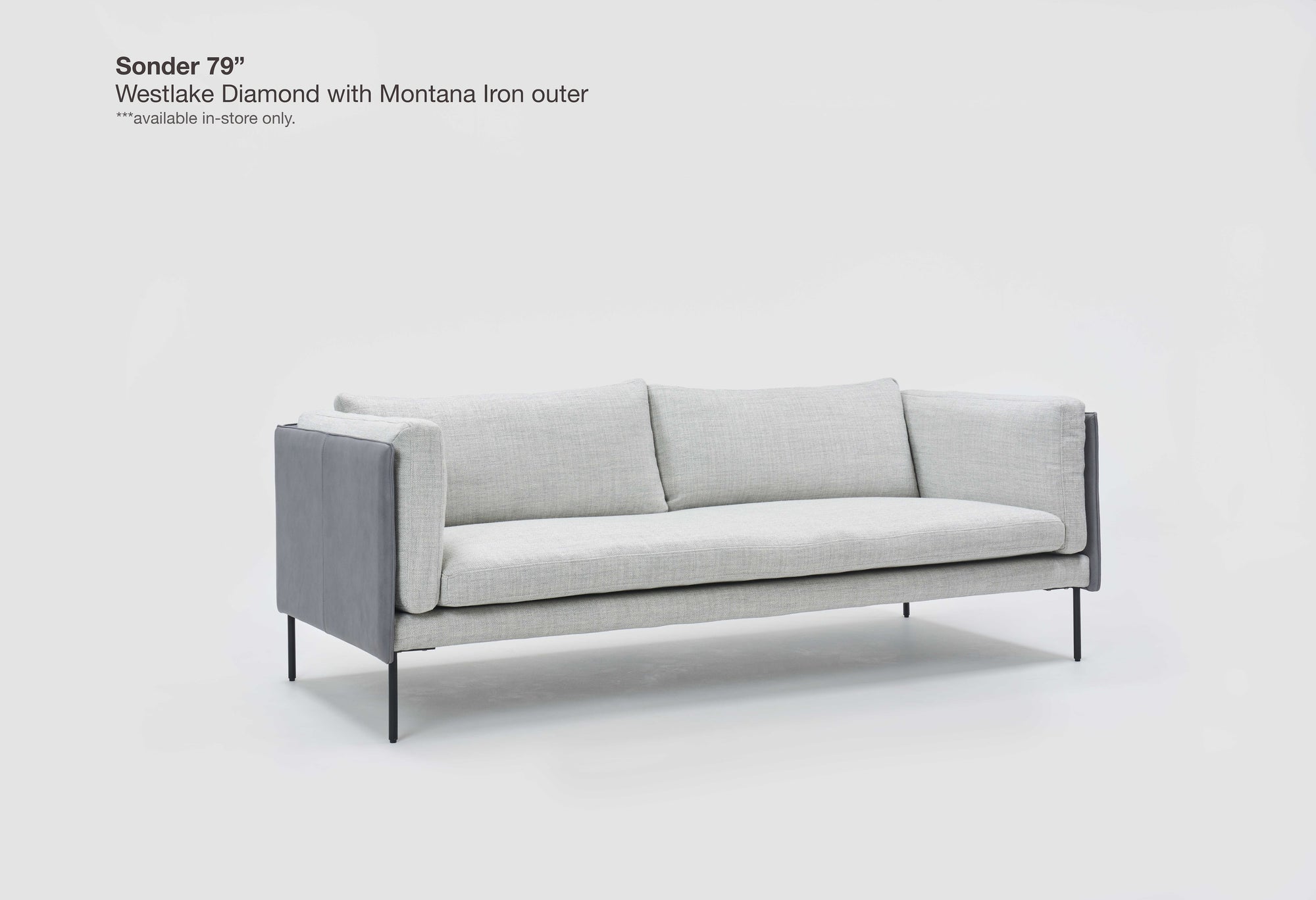 A modern Sonder Sofa | Fabric by Wooden Stories, featuring light gray upholstery, three plush feather-filled cushions, Danish-inspired lines, black metal legs, and armrests. Text in the corner reads: “Sonder 79”, Westlake Diamond with Montana Iron outer, available in-store only.