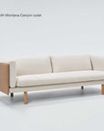 A modern beige three-seat sofa, the Sonder Sofa | Fabric by Wooden Stories, is displayed on a plain white background. With elegant Danish-inspired lines and a sleek linear frame complemented by wooden sides and legs, this design seamlessly blends timeless style with comfort. In the top left corner, text highlights the model name and upholstery details.
