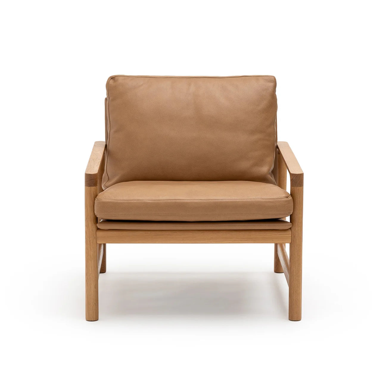 The Troubadour Lounge Chair by Wooden Stories features tan leather cushions and a light oak frame, inspired by Danish design. Shown from the front against a white background.
