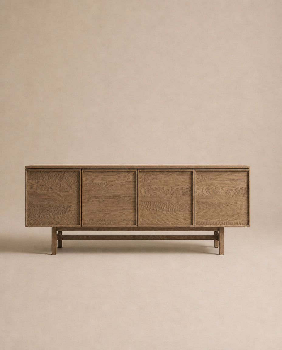 The Wooden Stories Yorke Sideboard features four panel doors and a minimalist design, showcased against a beige background. Its elegant Scandinavian-inspired style is highlighted by the visible grain of solid oak, while a simple rectangular base provides sturdy support.