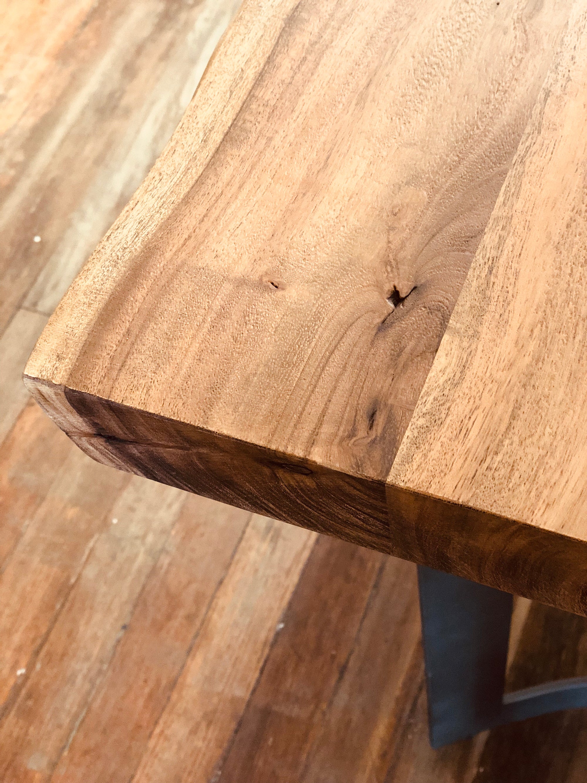 Close-up of the Leviathan Live Edge Counter Table by Moes, showcasing its rich acacia grain, knots, and texture. Set on a hardwood floor, the table highlights natural beauty with its distinctive live edge design.